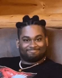 a man with braids is sitting on a couch smiling .