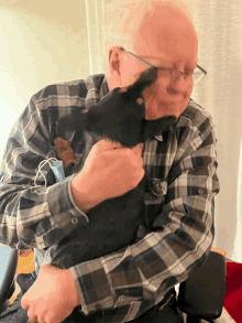 a man in a plaid shirt is holding a black cat