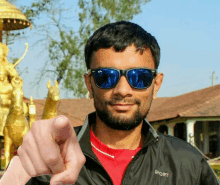 a man wearing sunglasses and a jacket that says sport pointing at the camera