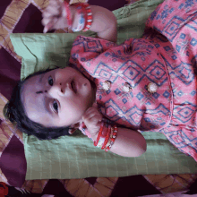 a baby wearing a pink dress and bracelets laying on a bed