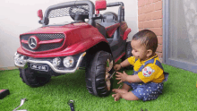 a baby is playing with a red mercedes jm-2188 toy car