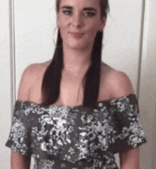 a woman is standing in front of a white wall wearing a floral off the shoulder dress .