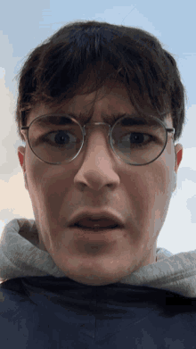 a young man wearing glasses and a hoodie makes a funny face