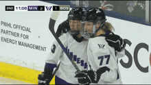 two female hockey players are hugging each other in front of a sign that says pwhl official partner for energy management