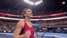 a woman in a pink tank top is holding a tennis racquet in a stadium with a wta logo in the background