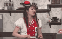 a woman in a red and white outfit is sitting at a counter in front of a shelf with bottles of aquafina water