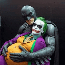 batman and the joker are hugging each other while the joker is holding a pregnant woman 's belly .