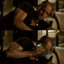 a bald man is laying on the floor holding a pile of money in his hands .