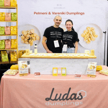 a man and woman stand behind a table with ludas dumplings written on it