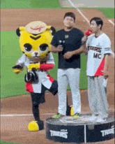 a tigers mascot is standing on a podium next to a man holding a microphone on a baseball field .