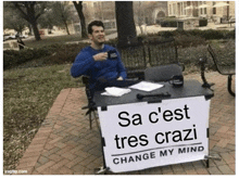 a man is sitting at a table with a sign that says sa c'est tres crazi change my mind