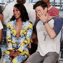 a man is covering his face with his hand while sitting next to a woman in a colorful outfit .