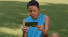 a young boy in a blue shirt is holding a piece of paper in his hands and reading it .