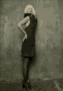 a woman in a black dress is standing in front of a grey wall