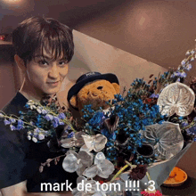 a young man holding a teddy bear and a bouquet of flowers with the caption mark de tom