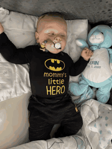 a baby with a pacifier in his mouth is wearing a batman shirt that says " mommy 's little hero "