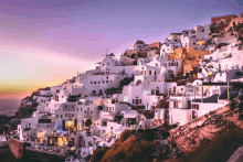 a row of white buildings on a hillside with a purple sky in the background