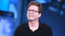 a man wearing glasses and a black shirt is smiling while standing in front of a blue background .