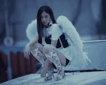 a woman wearing angel wings and knee high boots sits on the hood of a car