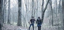 a man and a woman are standing next to each other in the woods .