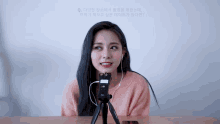 a woman wearing headphones and a pink sweater is sitting in front of a microphone on a tripod