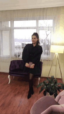 a woman in a black dress is standing next to a purple couch