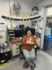 a woman sitting in an office holding a plate of pizza