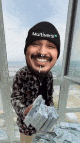 a man wearing a beanie that says multivers holds a pile of money