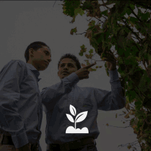 two men are looking at a plant and one of them is wearing a shirt that says " agricultura " on it