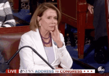 a woman in a white jacket is sitting in front of a live abc news address to congress sign ..