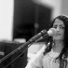 a woman is singing into a microphone while sitting in front of a piano .