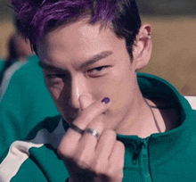 a man with purple hair is wearing a green jacket and a ring on his finger