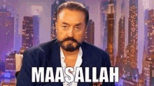 a man with a beard and mustache is sitting in front of a city skyline and says maaallah .