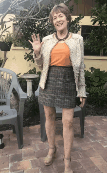 a woman wearing a plaid skirt and a white jacket is waving her hand