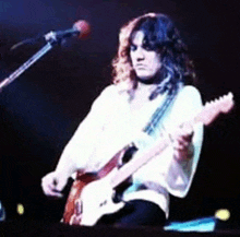 a man with long hair is playing a guitar in front of a microphone .