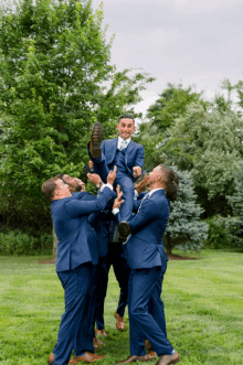 a man in a suit is being lifted in the air by his groomsmen in blue suits