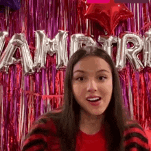 a woman is sitting in front of a red curtain with balloons in the shape of the word vampire on it .