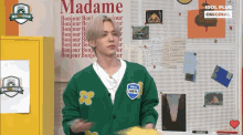 a man in a green cardigan stands in front of a wall with madame written on it