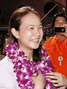 a woman is wearing a lei of purple flowers and smiling while a man takes a picture of her .