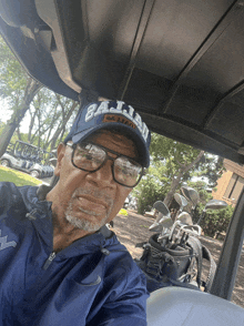 a man wearing glasses and a hat that says dallas is sitting in a golf cart