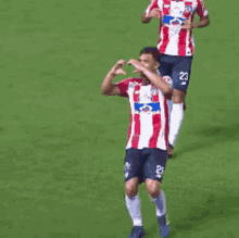 a man in a red and white striped shirt with the number 23 on his shorts is playing soccer on a field .