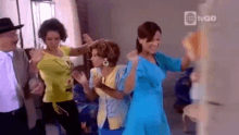 a group of women are dancing together in a room with a man in a hat .