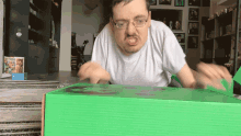 a man wearing glasses is opening a green box with the letter g on it