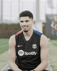 a man wearing a spotify tank top sits on a bench