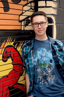 a young man wearing glasses is standing in front of a mural on a wall .