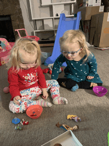 two little girls wearing glasses are playing with toys and one has a shirt that says ' christmas ' on it