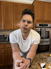 a man in a white shirt is sitting at a kitchen counter with his hands folded