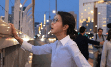 a woman wearing glasses and a white shirt reaches out to touch a fence