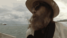 a man with a beard wearing a hat and sunglasses looks out over the ocean