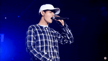 a man in a plaid shirt is singing into a microphone while wearing a white hat